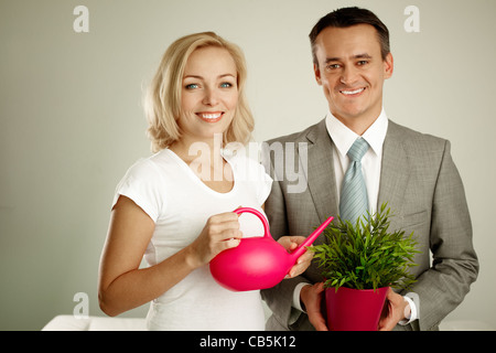 Photo de l'homme heureux avec plante et woman holding watering pot looking at camera Banque D'Images