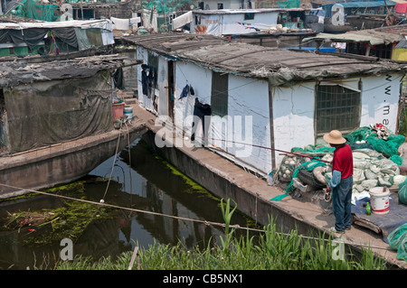 Chine, Jiangsu, Qidong, homme en chemise rouge et chapeau de paille avec une canne à pêche et la ligne de son bateau amarré dans un canal. Banque D'Images