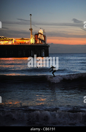 Les surfeurs profiter de la magnifique coucher de soleil comme ils attraper quelques vagues par le Palace Pier sur le front de mer de Brighton Banque D'Images