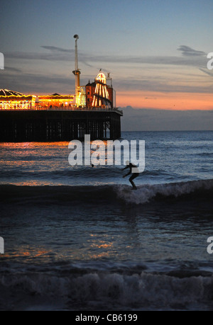 Les surfeurs profiter de la magnifique coucher de soleil comme ils attraper quelques vagues par le Palace Pier sur le front de mer de Brighton Banque D'Images