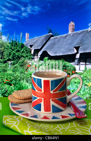Thé anglais Union Jack flag des tasse de thé et biscuits, chaumière typique et un jardin en arrière-plan UK Banque D'Images