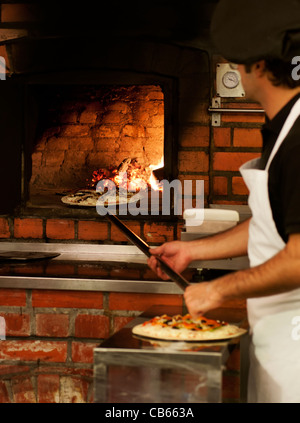 Un chef putting a pizza dans un four à bois dans le style italien classique Banque D'Images