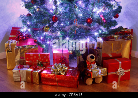 Photo d'un arbre de Noël avec des décorations et des lumières de fées entouré par présente sur un sol en bois Banque D'Images