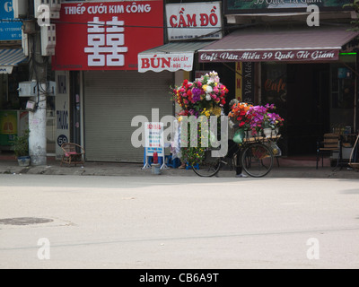 Marchande de fleurs sur un vélo chargé de fleurs dans une rue de Hanoi, Vietnam Banque D'Images