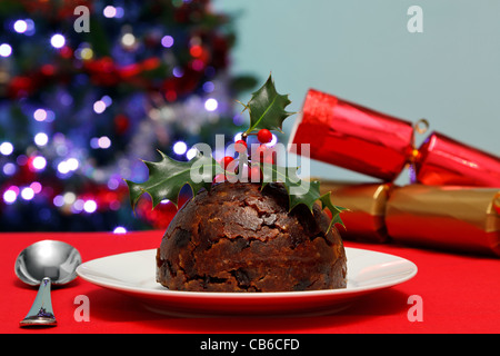 Photo d'un pudding de Noël avec le houx sur le dessus avec des craquelins et des arbres en arrière-plan. Banque D'Images