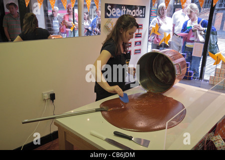 Avec une foule de spectateurs, une jeune femme fait un lot de fudge à la main dans l'atelier de fudge Roly sur le Watergate Street, Chester, Royaume-Uni. Banque D'Images