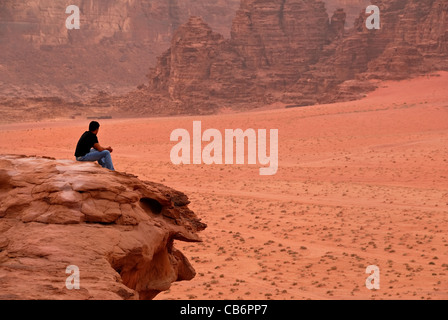 Un homme assis sur une falaise et profiter de la vue du désert de Wadi Rum dans le désert chaud de l'air. Banque D'Images