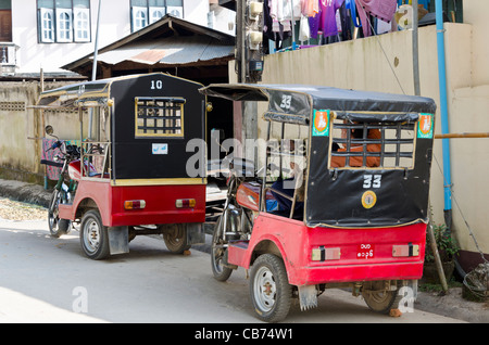 Deux birmans rouge & noir tuk-tuks stationné sur une rue de Tachileik Myanmar (Birmanie) Banque D'Images