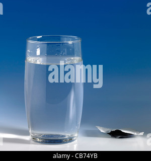Comprimé effervescent résolus dans un verre d'eau, le boîtier vide à côté. Tourné en studio blue back Banque D'Images