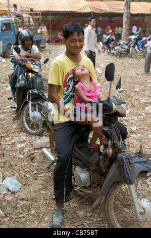 Smiling Cambodian man avec sa fille assise sur un cyclomoteur à une fête de village, nouvel an cambodgien (Chaul Chnam Thmey), Bakong Village, Siem Reap, Cambodge Banque D'Images