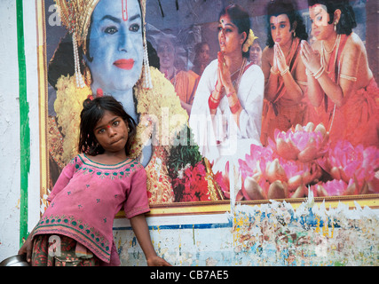 Les Indiens pauvres mendiant nomade Girl standing in front of a Rama sur une affiche de film Indian street. L'Andhra Pradesh, Inde Banque D'Images