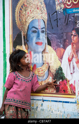 Les Indiens pauvres mendiant nomade Girl standing in front of a Rama sur une affiche de film Indian street. L'Andhra Pradesh, Inde Banque D'Images