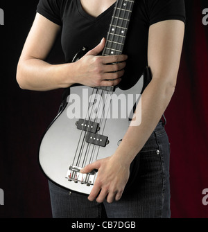 Détail d'une femme et d'un black bass guitare devant de dos rougeâtre en partie Banque D'Images