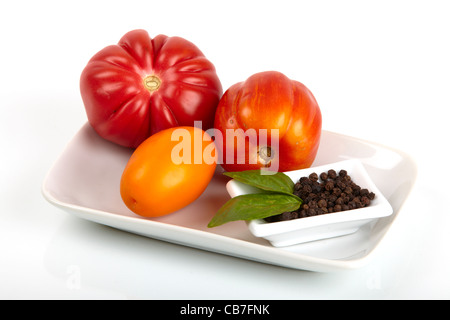 Différentes variétés de tomates biologiques et un plat de poivre et une feuille de basilic sur un plateau isolé sur fond blanc Banque D'Images