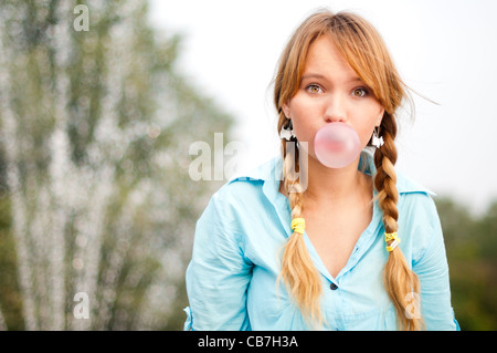 Beau jeune étudiant girl blowing bubble de chewing-gum et à la recherche dans l'appareil photo Banque D'Images