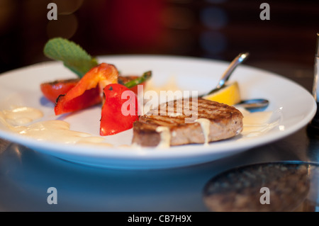 De délicieux steaks et légumes sur plaque blanche au restaurant avec fond coloré (très faible profondeur de champ) Banque D'Images