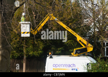 Un BT openreach ( / open reach ) jusqu'à un ingénieur a soulevé un palan afin qu'il puisse fixer un câble d'une maison jusqu'à l'poteau télégraphique. UK. Banque D'Images