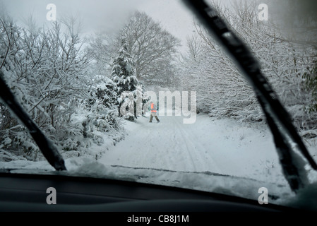 Conducteurs de route de neige POV vue d'hiver à travers le pare-brise de la voiture à la voie rurale dans la neige épaisse avec homme traversant dans la veste haute visibilité Banque D'Images