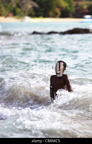 Un jeune garçon submergé la moitié surpris obtenir englouti par l'eau froide du surf à la plage de Nosy Komba, Madagascar, Afrique Banque D'Images