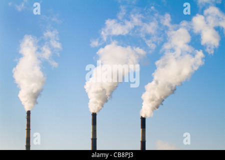 Les tuyaux de l'usine avec de la fumée contre le ciel bleu Banque D'Images