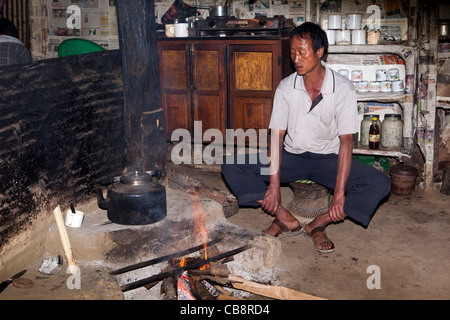 L'Inde, Nagaland, Jakhama Village, homme assis autour de feu de cuisson dans la cuisine de la maison de villageois Banque D'Images