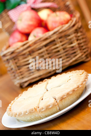 Tarte aux pommes sur une table en bois avec un panier de pommes en arrière-plan Banque D'Images