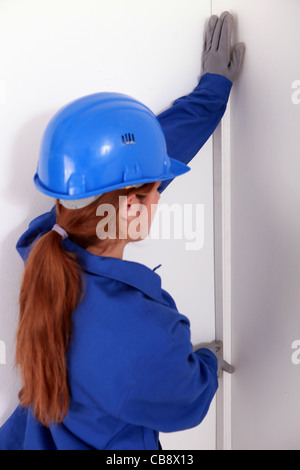 Le port d'un travailleur féminin jumpsuite bleu est le contrôle de la rectitude du mur Banque D'Images