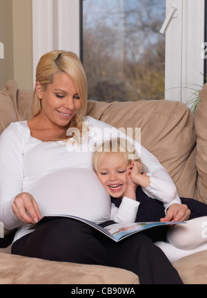 Heureuse mère enceinte et sa fille de trois ans la lecture d'un livre ensemble à la maison Banque D'Images