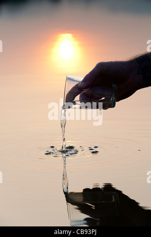 Verser un verre d'eau dans un lac encore au lever du soleil en Inde. Silhouette Banque D'Images