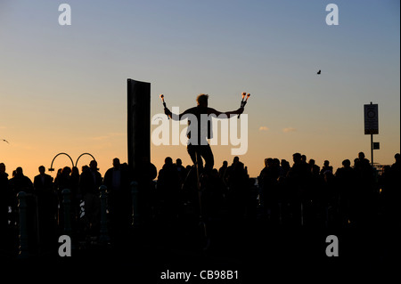 Regarder la foule une flamme juggling musicien ambulant sur un monocycle le long front de mer de Brighton pendant l'temps d'automne exceptionnellement doux Banque D'Images