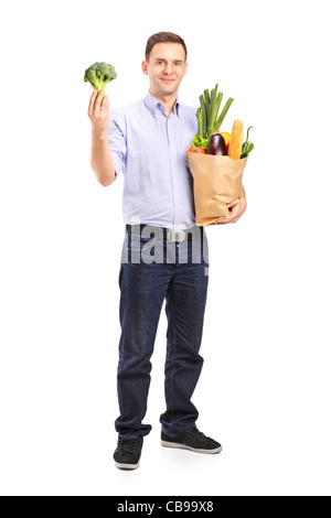 Jeune homme tenant un panier avec des produits et un brocoli dans sa main isolé sur fond blanc Banque D'Images