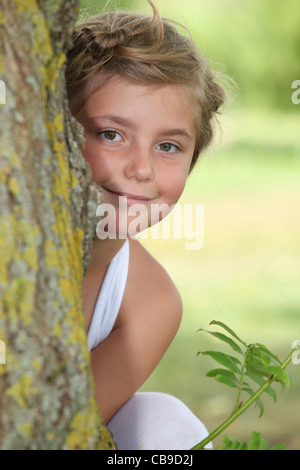 Jeune fille en robe blanche se cacher derrière un arbre Banque D'Images