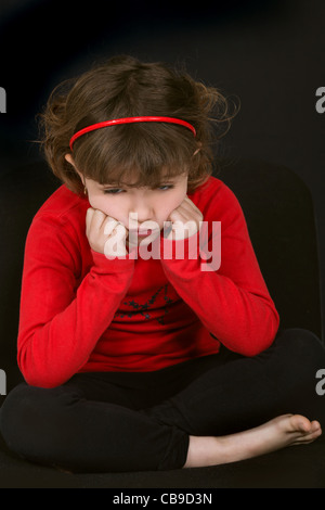 Petite fille tacaud avec face en appui sur les mains contre fond noir Banque D'Images