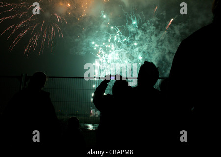 D'artifice à Londres, vert vif et explosions rouge alors que le ciel se découpant les gens recherchent de derrière une clôture Banque D'Images