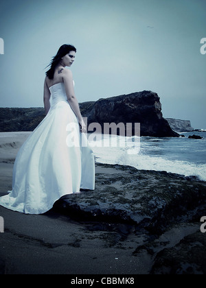 Une femme portant une robe de mariage sur une plage seul avec ressac Banque D'Images