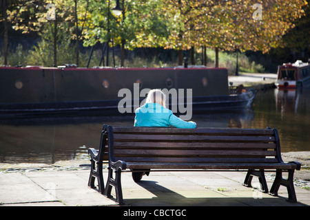 Une dame s'assoit la lecture au soleil sur un automne tranquille après-midi. Banque D'Images