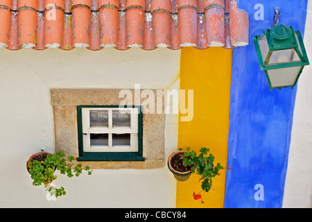 Fenêtre, lampe de rue et un toit en tuiles d'argile avec un mur de couleur pastel dans le village médiéval d'Obidos Banque D'Images