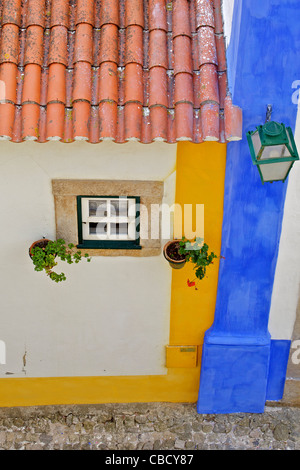 Fenêtre, lampe de rue et un toit en tuiles d'argile avec un mur de couleur pastel dans le village médiéval d'Obidos Banque D'Images