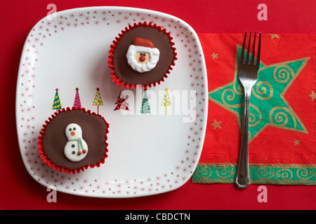 Le Snowman cupcake cupcakes et Santa des gâteaux sur la plaque de l'arbre de Noël et étoiles avec serviette fourchette sur fond rouge Banque D'Images