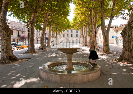 Une femme en passant par une fontaine dans un square bordé d'arbres à Gignac Gignac Hérault Languedoc-Roussillon France Banque D'Images