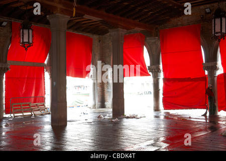 Ouvrier nettoyant le sol mouillé de l'arcade derrière des écrans de marché rouges, Venise Banque D'Images
