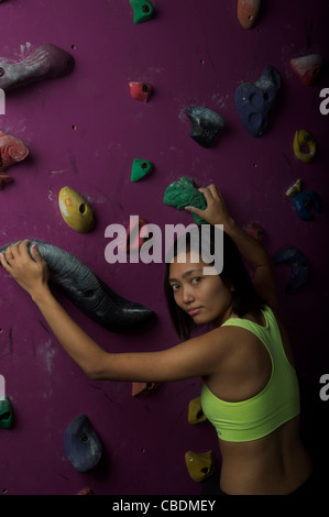 Jeune, athlétique et attrayant, l'escalade asiatique de la gir dans un centre artificiel d'escalade ou une salle de gym. Banque D'Images