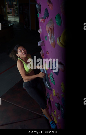 Jeune, athlétique et attrayant, l'escalade asiatique de la gir dans un centre artificiel d'escalade ou une salle de gym. Banque D'Images