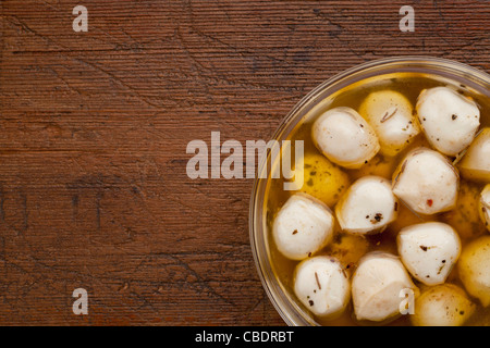 Boules de fromage mozzarella marinés dans l'huile d'assaisonnement, bol en verre sur fond de bois patiné Banque D'Images