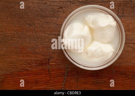 Trois boules de fromage mozzarella frais dans un bol en verre sur la surface de bois grunge rayé Banque D'Images