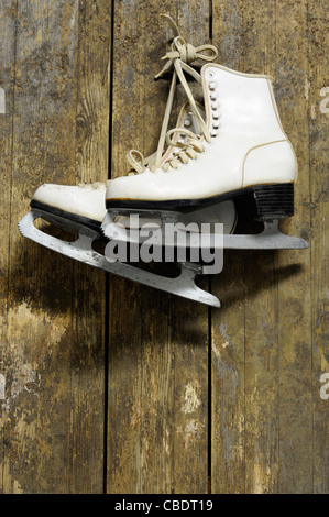 Patins à glace blanc accroché sur un vieux mur en bois patiné Banque D'Images