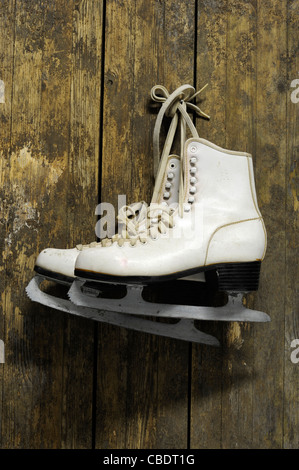 Patins à glace blanc accroché sur un vieux mur en bois patiné Banque D'Images