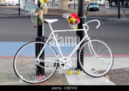 Vélo de couleur blanche memorial et fleurs pour cycliste tué à la jonction de route comprend blue voie cyclable marquage routier Banque D'Images