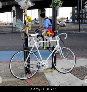 Vélo de couleur blanche memorial et fleurs pour cycliste tué à la jonction de route comprend blue voie cyclable marquage routier Banque D'Images