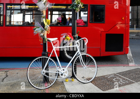 Vélo de couleur blanche memorial et fleurs pour cycliste tué à la jonction de route comprend blue voie cyclable marquage routier Banque D'Images